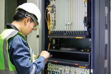 Network technician performing inspection on server equipment with safety helmet and vest in data center room focused on maintenance task