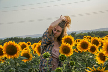young blond woman among sunflowers in the field, doing her hair, straightening her hair with her...