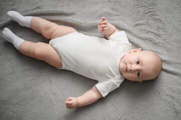 Cute baby lying on back in crib after waking up, top view. Baby awake in crib looking around and...