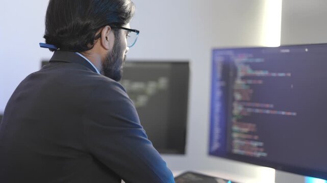 Indian male software architect developing a neural network framework. Focused programmer writing optimized code for a deep learning algorithm at a multi-display workstation.