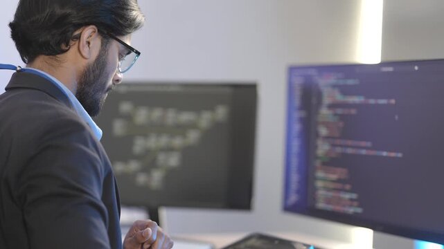 Focused Indian male AI developer coding a complex machine learning algorithm late at night. A dedicated data scientist working on a neural network at a multi-monitor workstation.