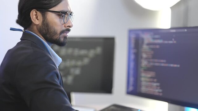 Indian male software architect developing a neural network framework. Focused programmer writing optimized code for a deep learning algorithm at a multi-display workstation.