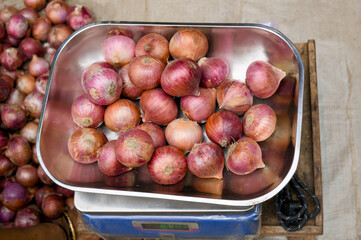 Fresh red onions displayed on a weighing scale in market