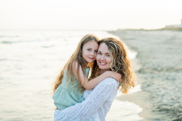 Young mother with little daughter near the sea. Beach with sand. Blue water.