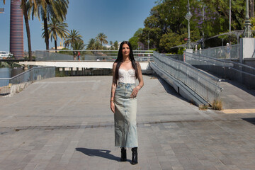 A young, attractive Latin woman with tattoos on her arms and dressed in casual clothes walks and...