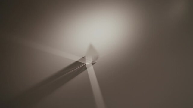 Top view of light refracting through triangular glass prism, splitting into vibrant color spectrum, casting sharp shadow against gray surface of table, demonstrating optical physics principles closeup