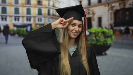 Young caucasian woman in graduation uniform smiling on city street during outdoor ceremony,...