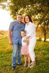 Happy family spending time outdoors standing at sunset in park. Mom, dad and daughter relaxing...