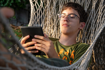Teenager boy reading on an e-reader while relaxing in a hammock outdoors