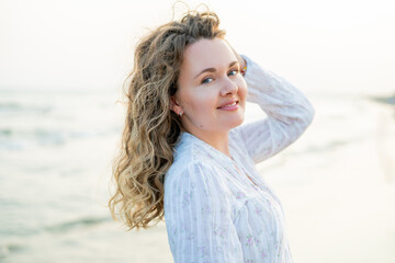 Young curly woman near the sea. Beach with sand. Blue water.