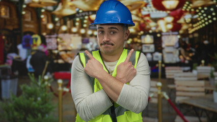 Young man in reflective vest and hardhat pointing with fingers on a lively city street, offering a vibrant depiction of urban outdoor settings with an engaging expression.