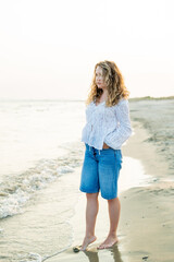 Young curly woman near the sea. Beach with sand. Blue water.