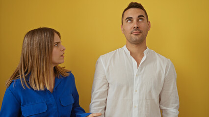 Woman looking at man against vibrant yellow background expressing emotion together in isolated...