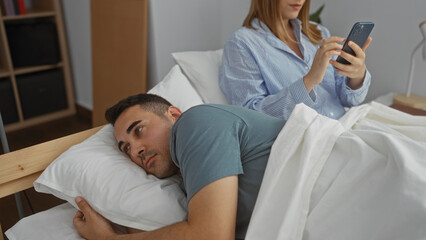 Obraz premium Couple in bed with woman using phone while man looks away reflecting on relationship in cozy bedroom setting indoors during morning light together happy love serene calm.