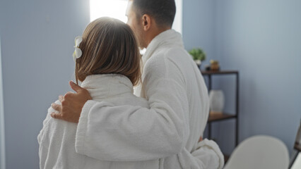 Obraz premium Couple embracing in cozy spa room wearing white robes reflecting relaxation and wellness in a serene, indoor setting, embodying love, connection, and a peaceful atmosphere.