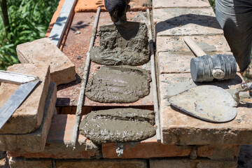 A hand applies mortar with a trowel to prepared brick surfaces for the next layer