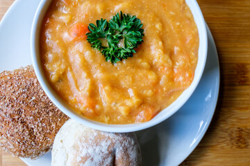 A Bowl Of Hot Lentil Soup Garnished With Parsley With Bread Rolls
