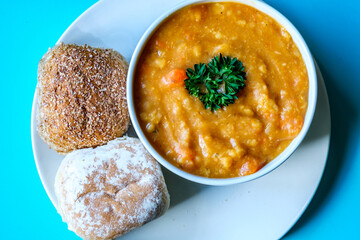 A Bowl Of Hot Lentil Soup Garnished With Parsley With Bread Rolls
