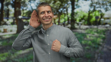Caucasian man listening with hand to ear and expressing emotions in an outdoor park setting.
