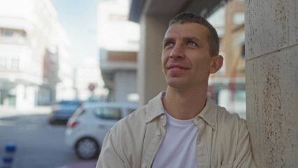 Obraz premium Man smiling against a wall in an urban street setting on a sunny day, portraying a sense of optimism and contentment in the city environment.