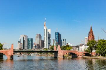 Fototapeta premium A Frankfurt city skyline in Germany with a bridge over a Main river. The bridge is red and the water is calm. Against the background of the blue sky.