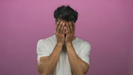 Man wearing white t shirt holding head between both hands and closing eyes in a studio with bright...