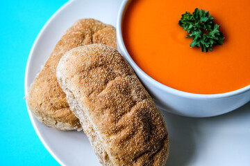 A Bowl Of Healthy Tomato Soup With Parsley Garnish And Wholemeal Submarine Bread Rolls
