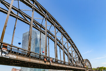 Fototapeta premium View of the railway bridge in Frankfurt, Germany, from the Main River A high-rise building and blue sky are visible in the background.