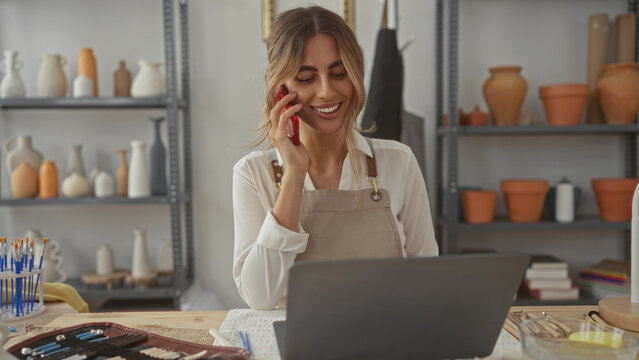 Young blonde woman holds phone in a pottery studio; creativity entrepreneurship concentration inspiration.
