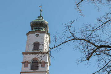 Fototapeta premium White church tower with a dome on top in Lindau, Germany An iron flag hangs on top On the right in the photo you can see a tree without leaves