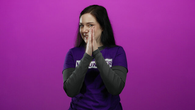 Woman brunette clapping happily in volunteer shirt against vibrant pink background exudes joy and commitment highlighting volunteerism and positivity making it ideal for nonprofit themes