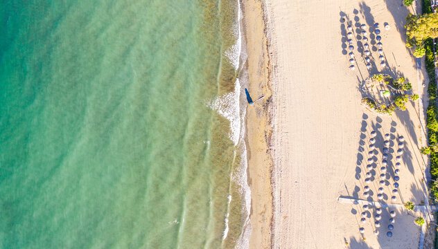 Aerial view of the sun-kissed shorelines meet the azure sea, a sandy expanse dotted with neat rows of beach umbrellas, Sierra de las Nieves, Andalusia, Spain.