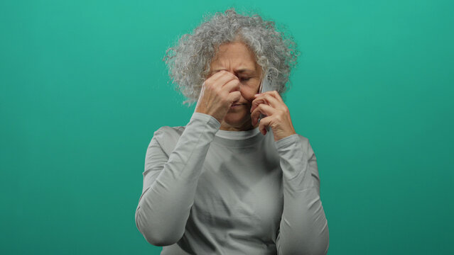 Woman with grey hair holding a phone looks stressed against a green background, suggesting a tense conversation or difficult news reception, emphasizing emotion and isolation. - Powered by Adobe