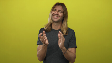 Blond man smiling and clapping hands in a vibrant yellow studio; support appreciation celebration...