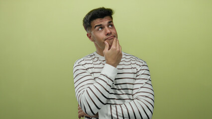 Young man pondering thoughtfully against a yellow background, wearing a striped shirt, embodying an introspective and curious demeanor.