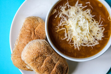 A Bowl Of Traditional French Onion Soup Topped With Grated Cheese And Wholemeal Submarine Bread Rolls