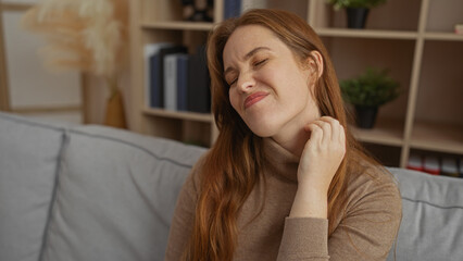 Naklejka premium Woman with red hair relaxes in comfortable home living room appearing thoughtful and serene.