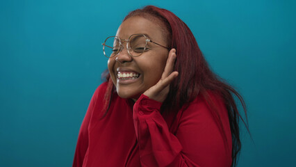 Woman with red hair wearing glasses and red shirt holding hand to ear listening in studio;...