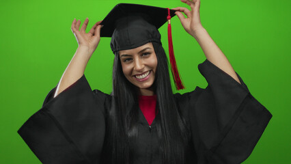 Young hispanic woman in graduation uniform smiling joyfully against isolated green background...