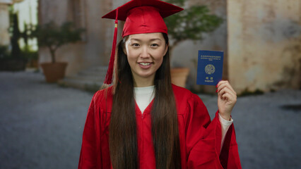 Woman in graduation gown happily holds korean passport outdoors on a city street symbolizing new...