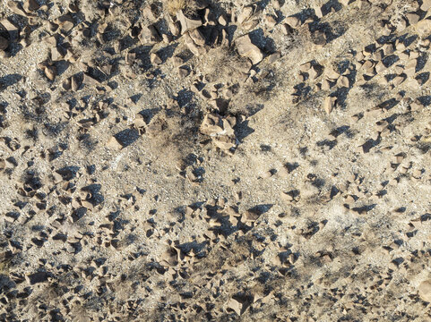Aerial view of arid landscape with scattered dark rocks casting shadows across the light-colored ground, creating a textured tapestry from above, Keetmanshoop, Karas Region, Namibia.