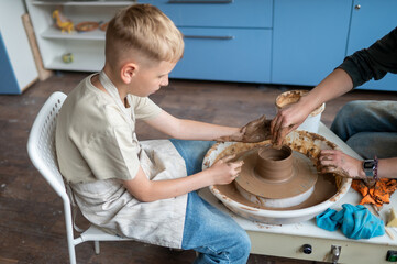 Child and instructor shaping clay together at pottery workshop