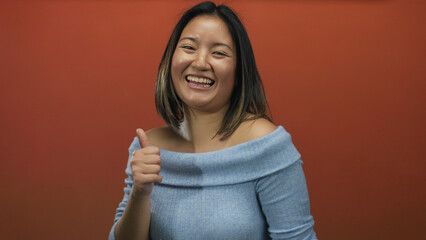 Woman smiling giving thumbs up against vibrant red wall signifying positivity and confidence