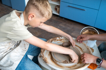 Child and instructor shaping clay together at pottery workshop