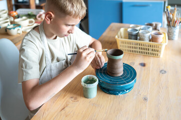 Focused boy painting ceramic cup at home pottery studio