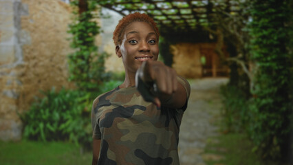 Military clad woman wearing camouflage tshirt finger pointing to camera in building entrance;...