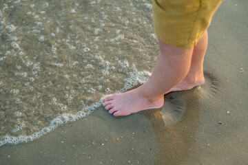 Closeup of children's feet near the sea. Beach with sand. Blue water.