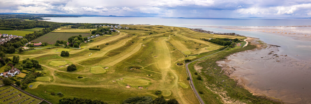 Aerial view of the verdant golf course meets the shimmering sea under a sky heavy with impending rain near the coastline, Aberlady, Scotland, United Kingdom.