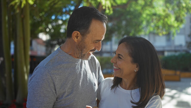 Hispanic couple enjoying a sunny day in an urban park, showcasing middle-aged love and connection in a vibrant city outdoors setting. - Powered by Adobe