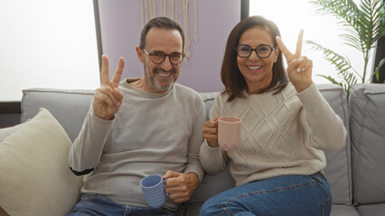 Hispanic couple enjoying a cozy moment in their living room sipping coffee, man and woman smiling...